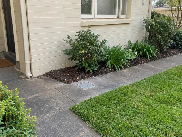 Flush inspection cover in paved garden path beside cream brick house in Artarmon